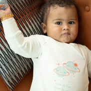 Baby wearing a onesie with a planet design, lying on a brown surface.