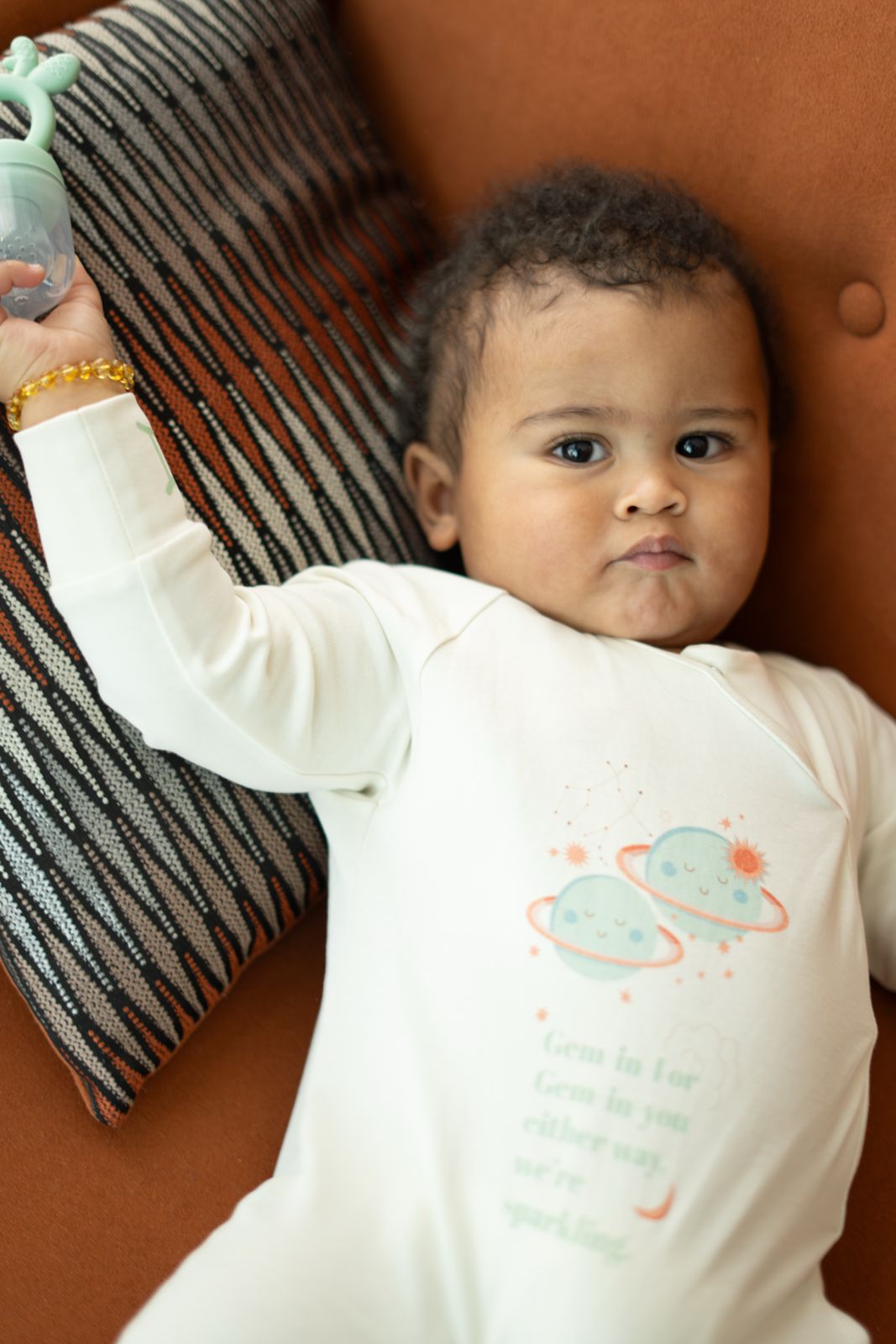 Baby wearing a onesie with a planet design, lying on a brown surface.
